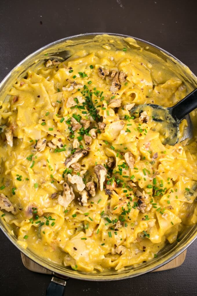 Overhead view of creamy pumpkin pasta in a steel skillet with fresh herbs and toasted walnuts.