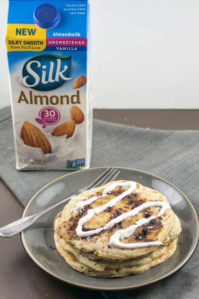 Stack of cinnamon swirl pancakes on a plate with a fork, with a carton of dairy-free almond milk in the background.