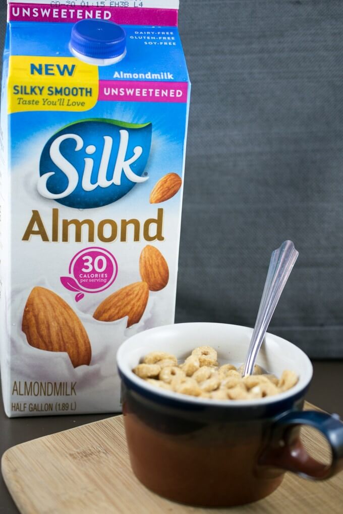 Silk® Unsweetened Almondmilk in a carton next to a mug with oat cereals and milk in it.