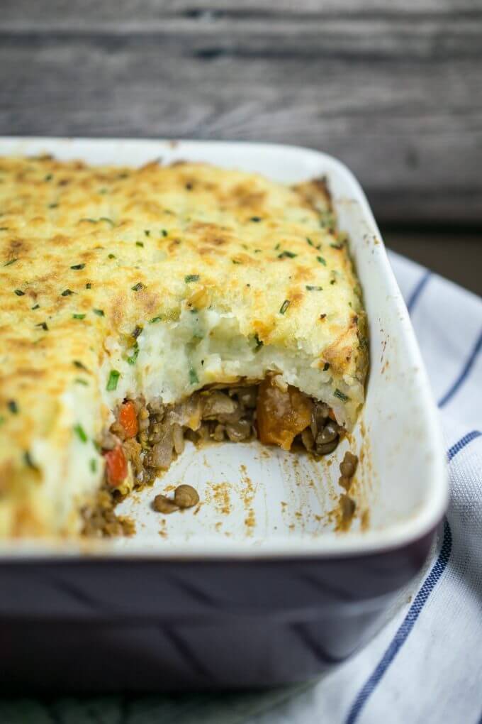 Inside view of vegan shepherd's pie, with a juicy layer of lentils and vegetables, topped with creamy mashed potatoes flecked with chives.