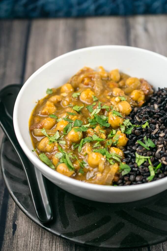 Coconut chickpea curry in a white bowl with forbidden rice and fresh coriander, atop a patterned black plate