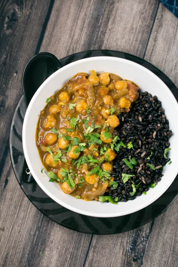 Overhead view of coconut chickpea curry, black lentils, quinoa, and fresh coriander in a bowl with a black spoon.