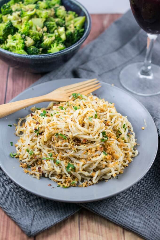 Shirataki spaghetti twirled together with browned toasted breadcrumbs and garlic olive oil sauce, garnished with parsley with a bowl of broccoli in the background.