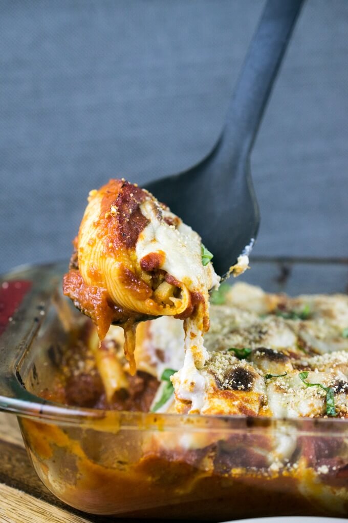 A vegan stuffed shell being scooped out of a casserole dish with stretchy cashew mozzarella coming off of the shell