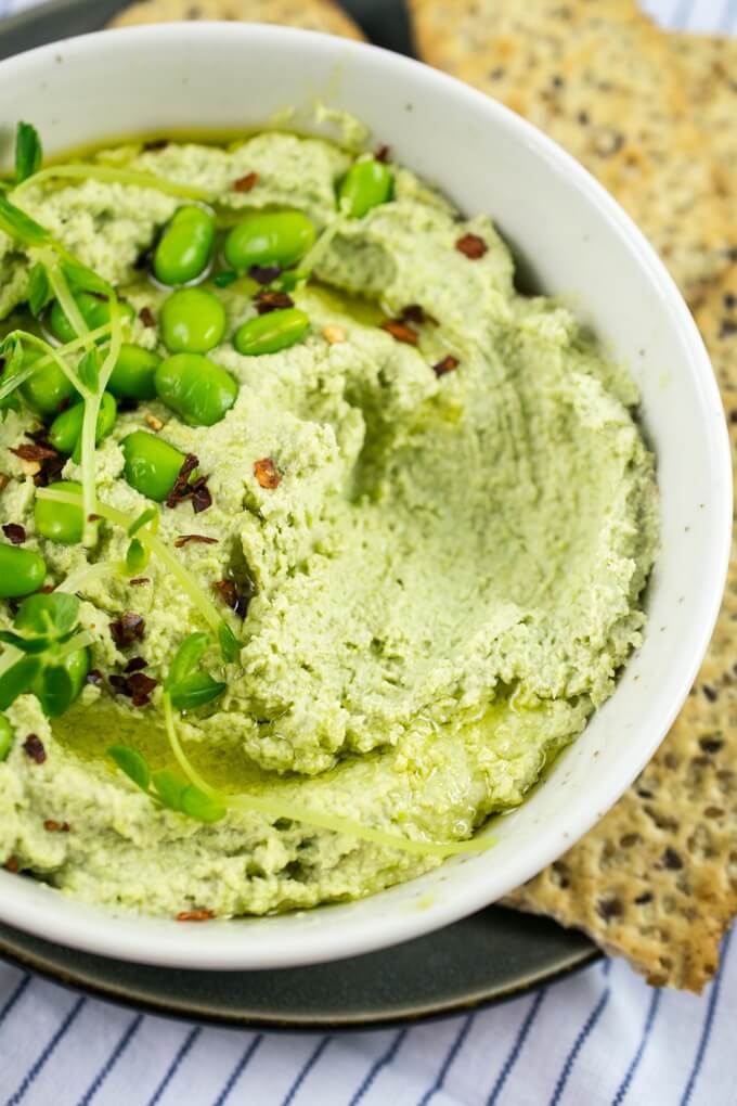 View of edamame hummus in a bowl with a visible area in the hummus where a cracker had been dipped into it.