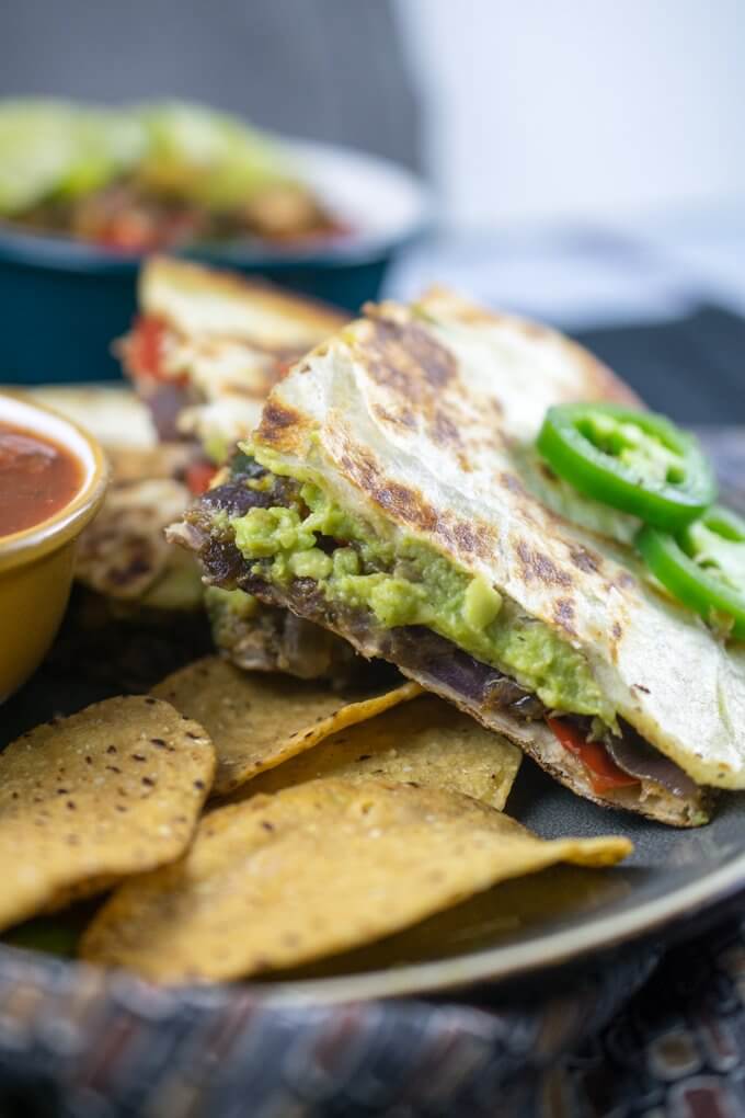 Close-up of the inside of a vegan quesadilla, with mashed avocado and a layer of spread refried beans, and sliced jalapeno for garnish.