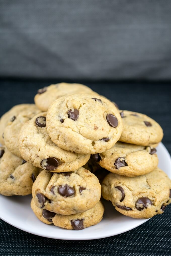 Front view of a stack of vegan chocolate chip cookies on a white plate on a dark gray table with a gray background