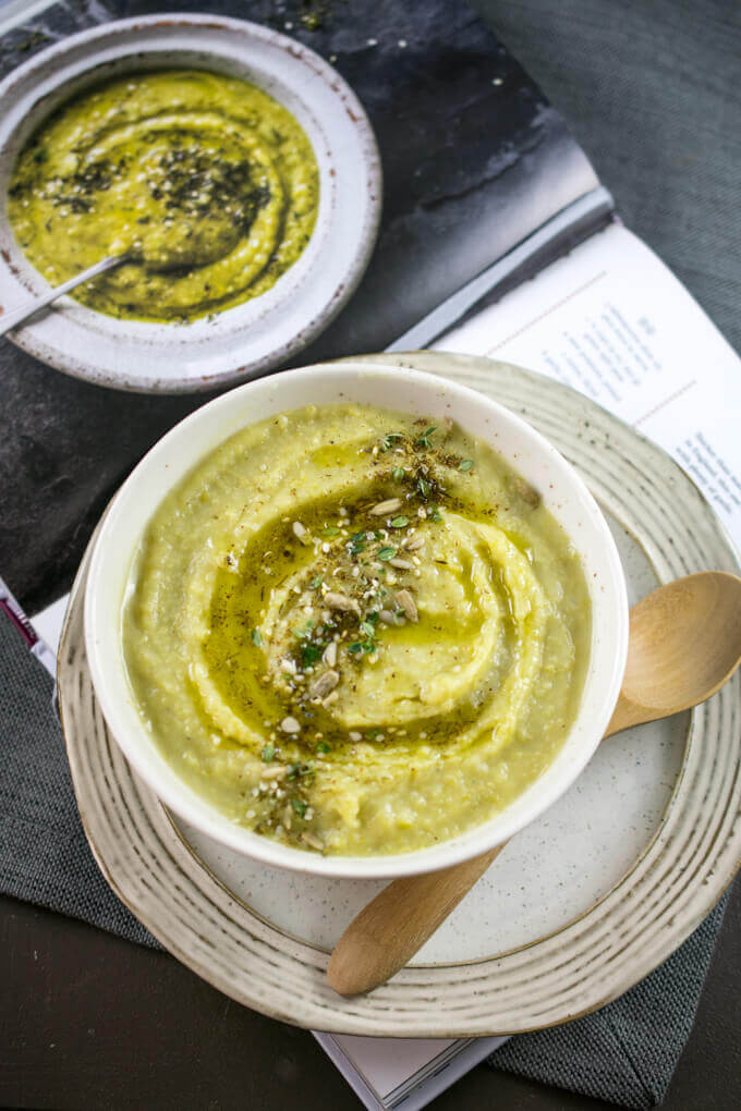 Lebanese green split pea soup in a ceramic bowl with a wooden spoon and plate, placed on top of the Middle Eastern Vegetarian Cookbook
