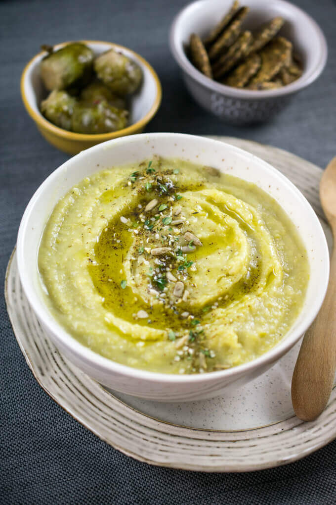 A bowl of vegan Lebanese green split pea soup, with a drizzle of olive oil on top and a generous sprinkling of za'atar herb and spice blend across the center of the bowl.
