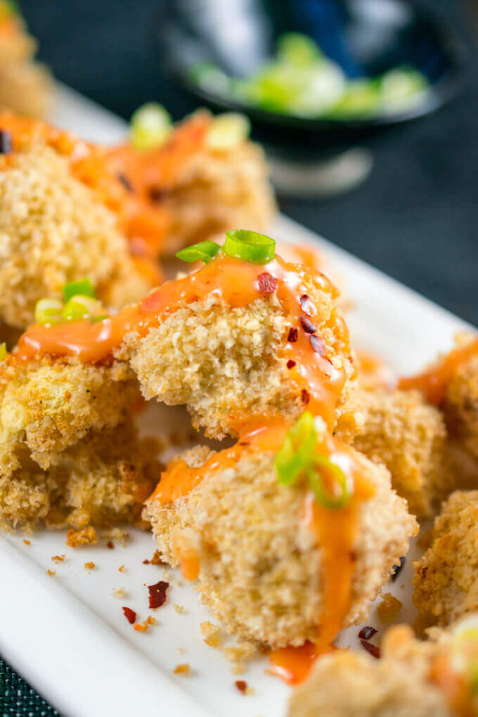 Close-up of a piece of breaded cauliflower drizzled with sweet chili mayo, and garnished with green onions and red pepper flakes