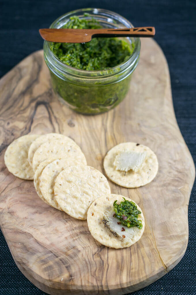 An assembled cashew cheese, cracker, and carrot top pesto platter on a wooden plank