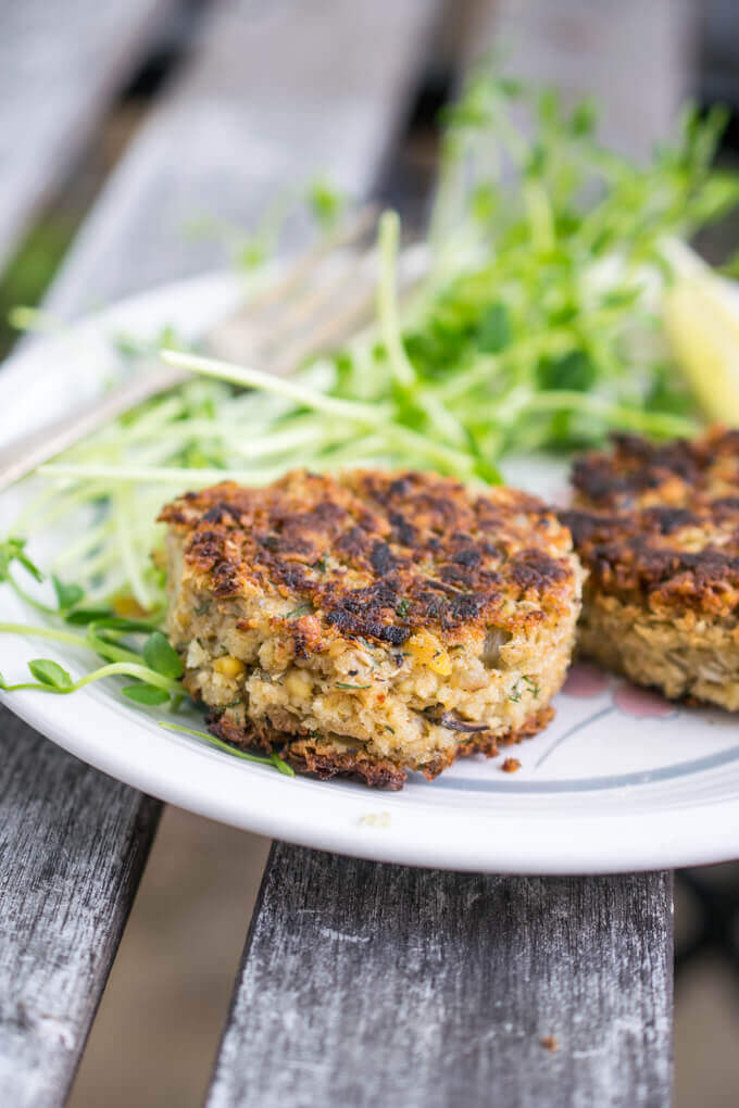 Vegan crab cakes on a plate with pea shoots in the background. Flecks of fresh dill are visible in the interior of the cake.