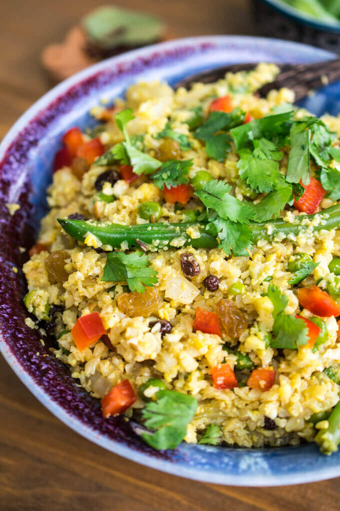 Close-up of cauliflower rice biryani with visible pieces of raisins, currants, bell pepper, clove, and peas