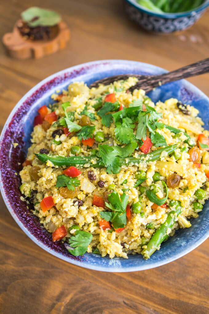 A ceramic bowl of yellow cauliflower rice with green beans, fresh cilantro, and pieces of fresh bell pepper