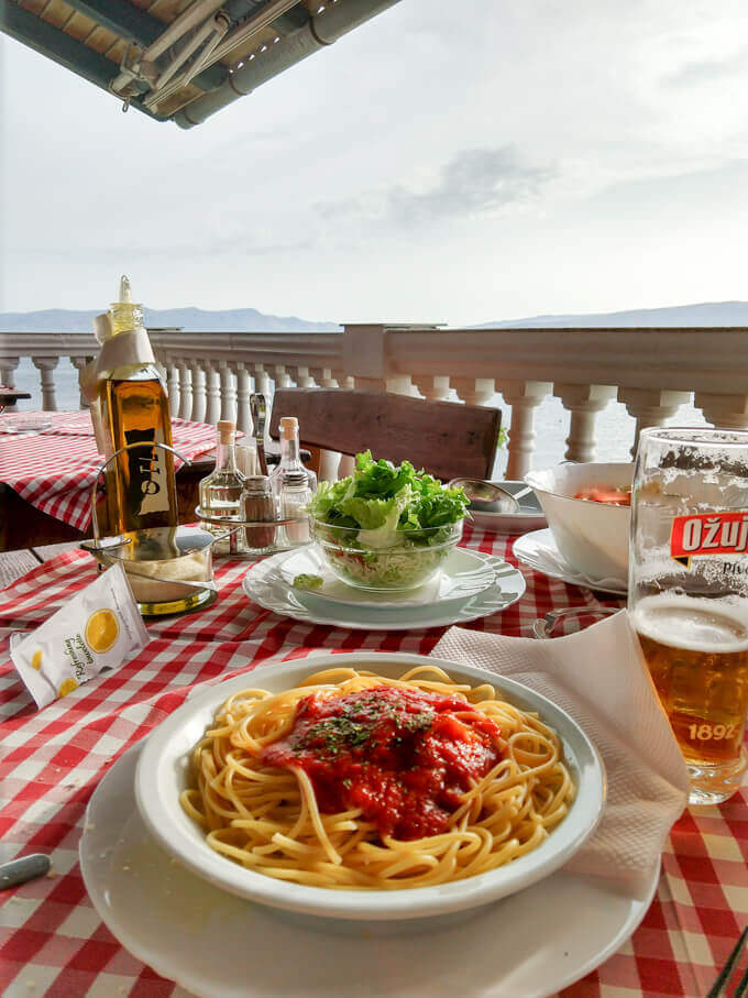 Table setting at a restaurant in Senj, Croatia with spaghetti napolitano, beer, and fresh salad