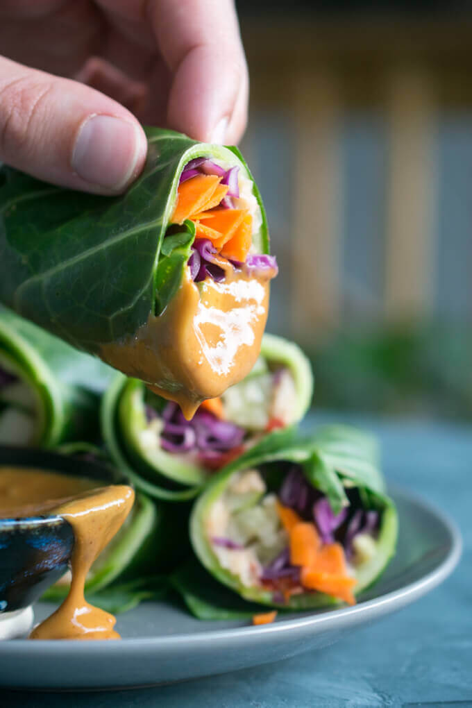 Close-up of a vegan collard wrap being dipped in Thai peanut sauce