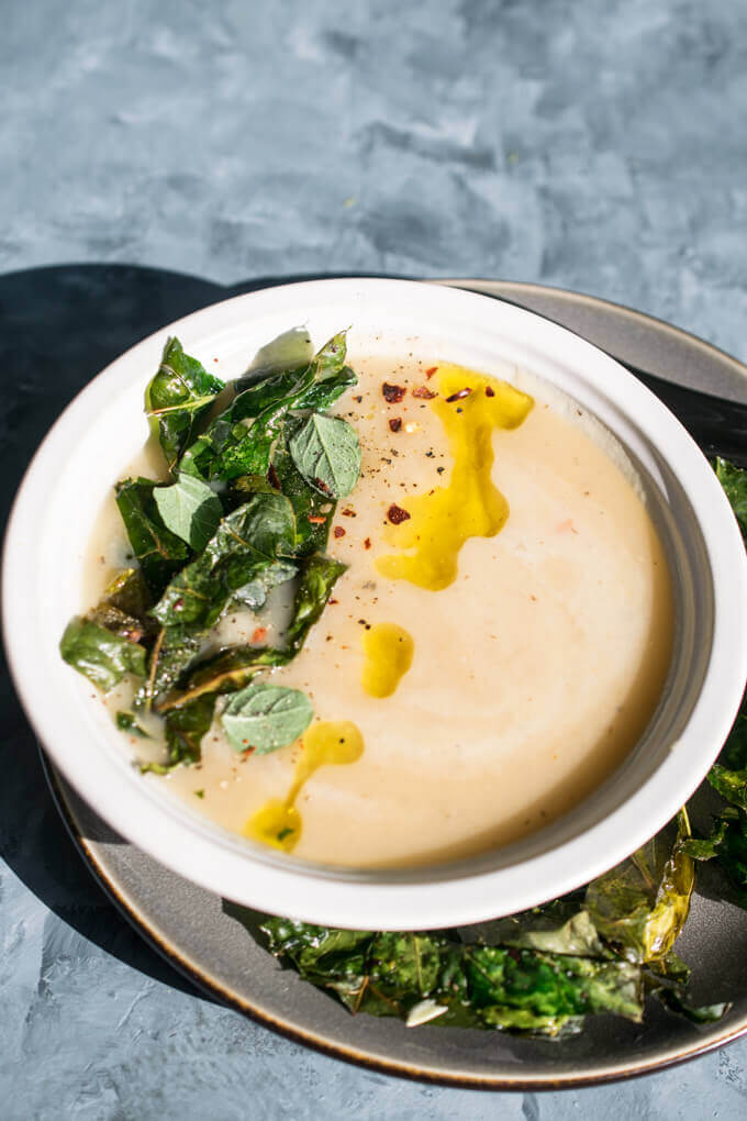 A bowl of creamy kohlrabi soup garnished with fresh oregano and crispy kohlrabi greens