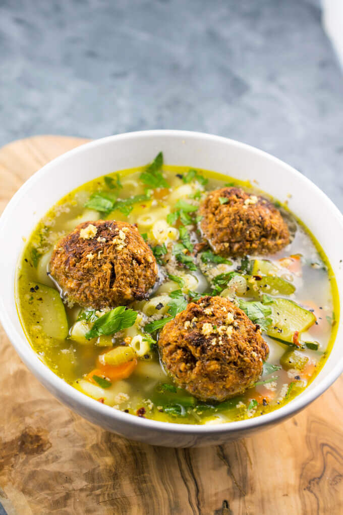 A bowl of summer vegetable minestrone with three vegan lentil balls placed on top