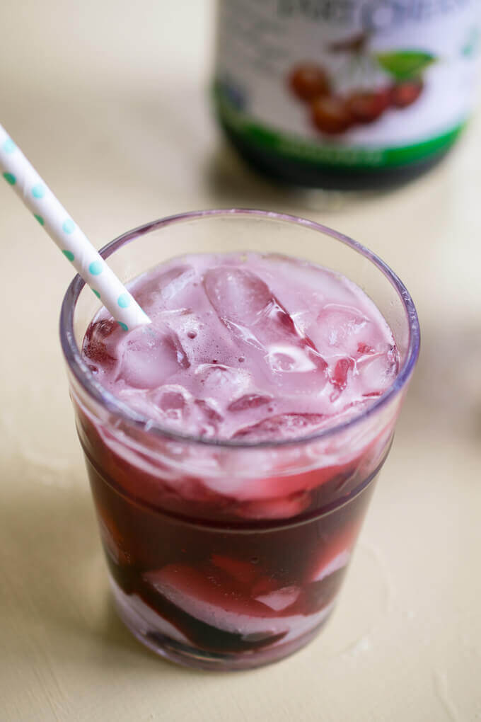 A tart cherry ginger cooler with visible carbonation on the surface and a polka dot straw.