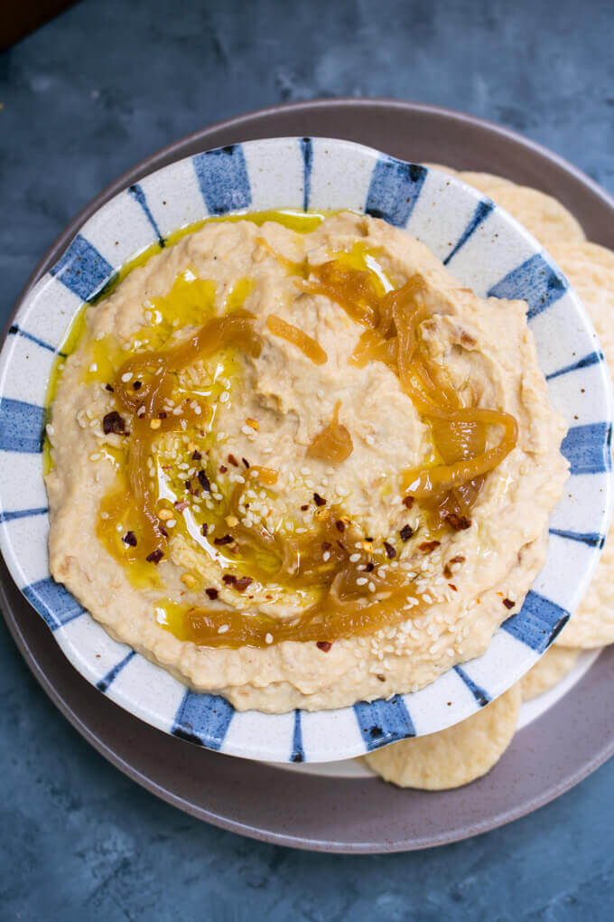 Creamy caramelized onion hummus in a blue ceramic bowl, topped with caramelized onions