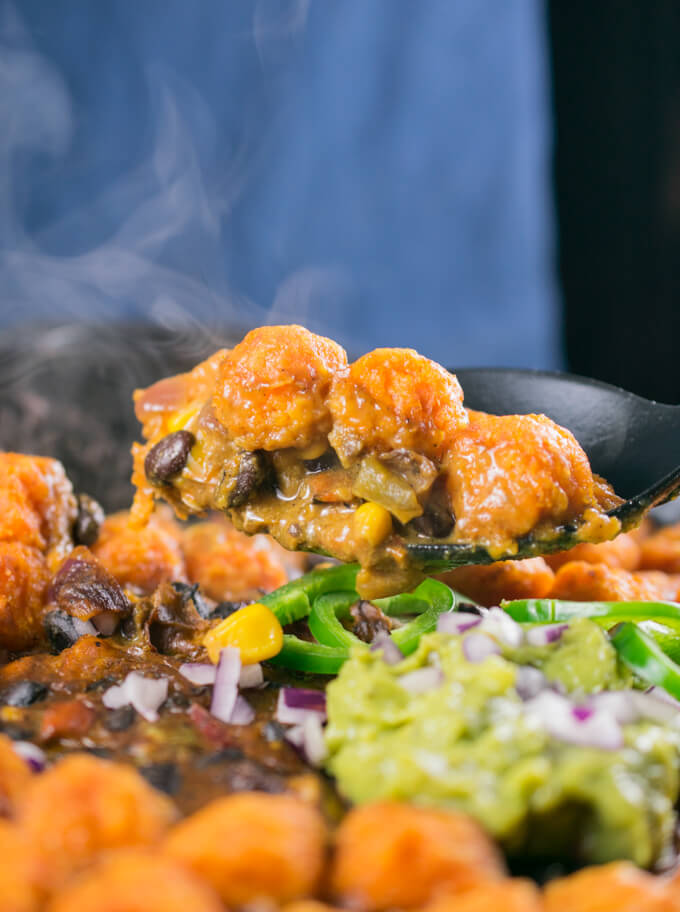 A scoop of vegan sweet potato tater tot hotdish, showing the cheesy texture of the inside of the casserole