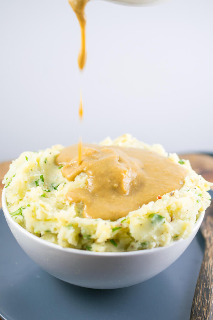 A bowl of fluffy vegan mashed potatoes with gravy being poured over them