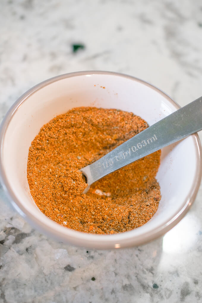 Mixed up homemade taco seasoning in a small bowl, showing a bright orange color with flecks of oregano and chili flakes.