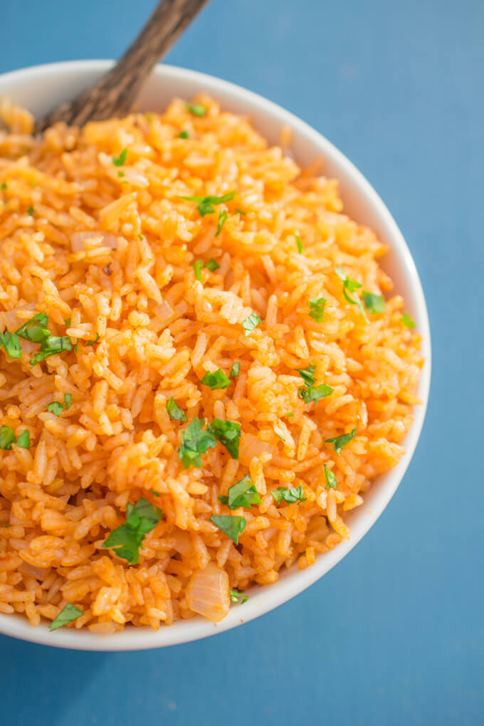 Close-up of Instant Pot Mexican rice in a white bowl, showing a bright orange color with flecks of onion, on a sky blue background.