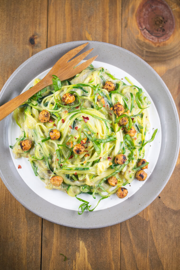 Overhead view from further away of a serving on a plate of one pot creamy garlic zucchini noodles on a wooden table