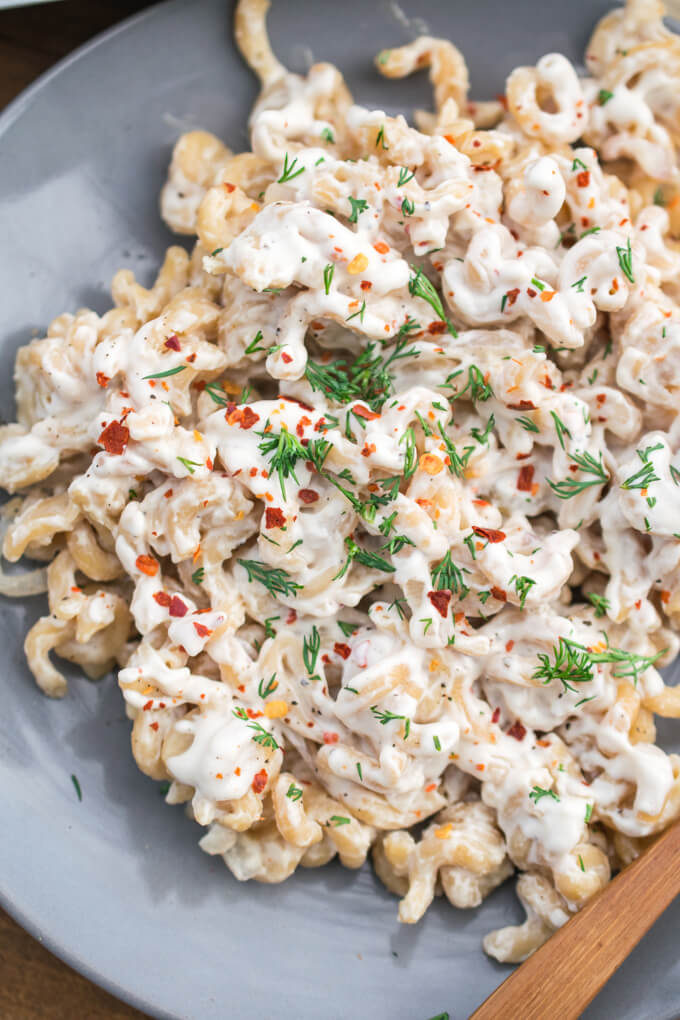 A plate of light pink lentil pasta spirals dressed with a creamy white lemon garlic sauce.