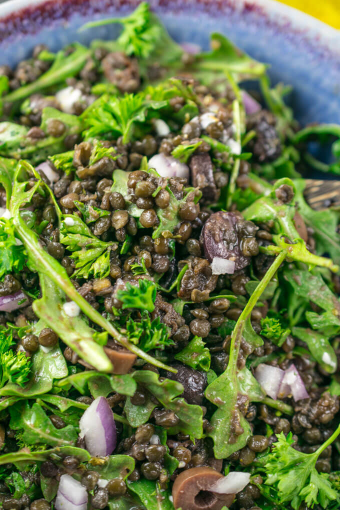 Close-up of lentil salad showing round black lentils, juicy kalamata olives, fresh parsley leaves, and arugula pieces.
