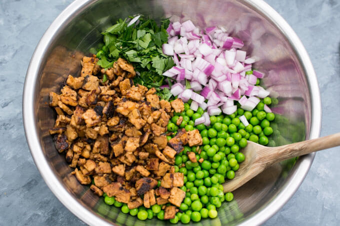Red onion, green peas, tempeh, and parsley in a bowl before being mixed
