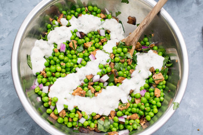 Ranch dressing being drizzled over the mixed vegan pea salad ingredients