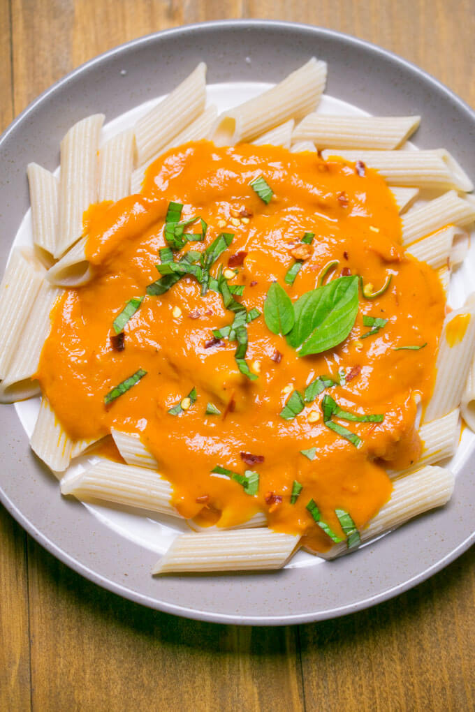Cooked penne pasta on a plate topped with creamy orange roasted tomato sauce and fresh basil leaves