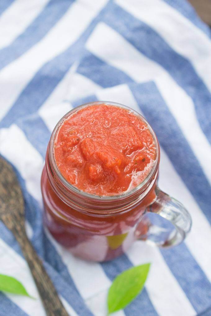 Oil-free marinara in a jar atop a blue and white striped napkin with fresh basil leaves scattered around.