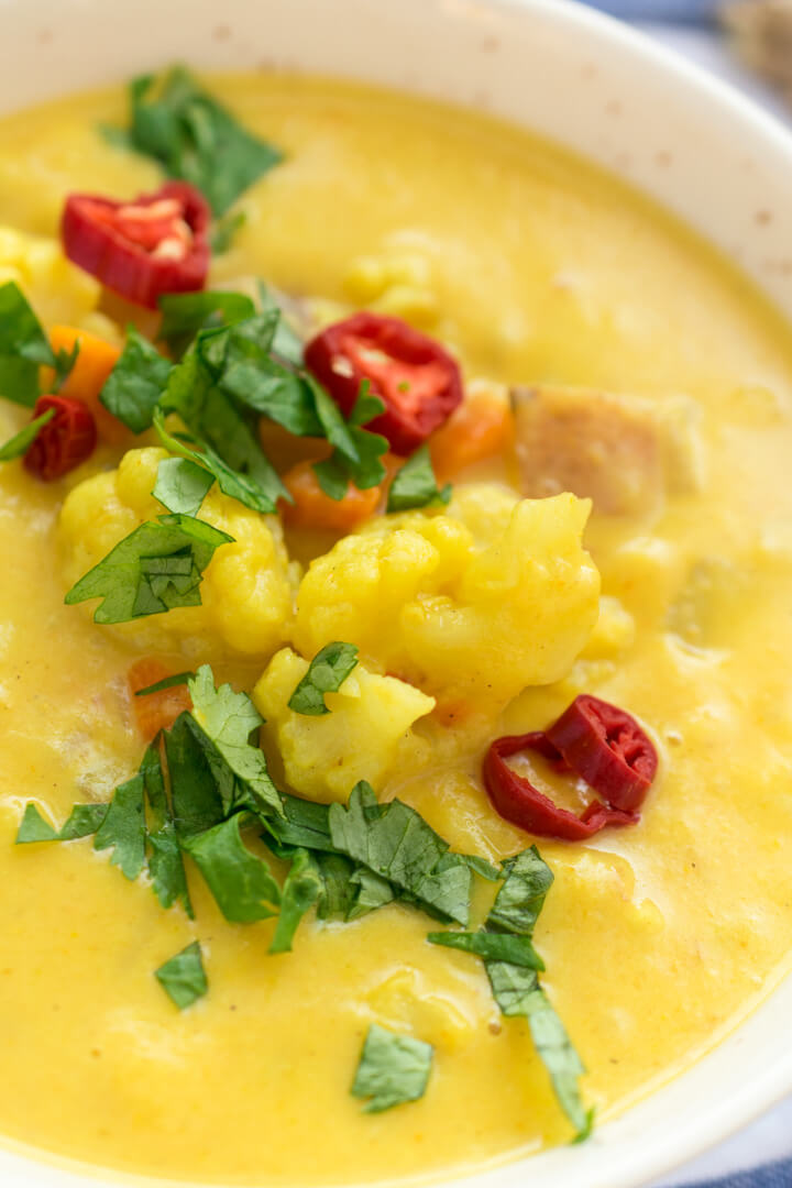 Close-up of vegan curried cauliflower chowder garnished with cilantro and red peppers.