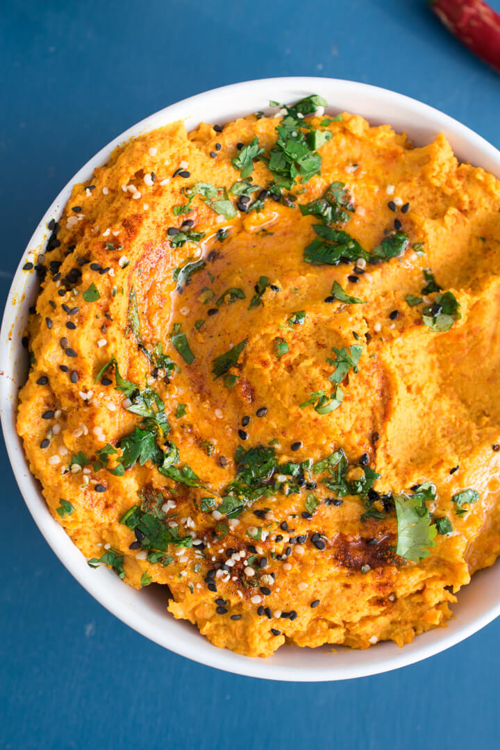 Close-up of ginger and roasted carrot hummus in a bowl, showing the bright orange color and smooth texture