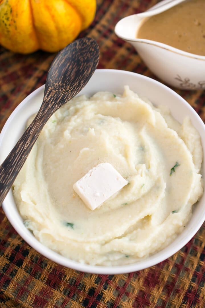 Vegan mashed cauliflower in a white bowl with a pat of dairy-free butter on top.