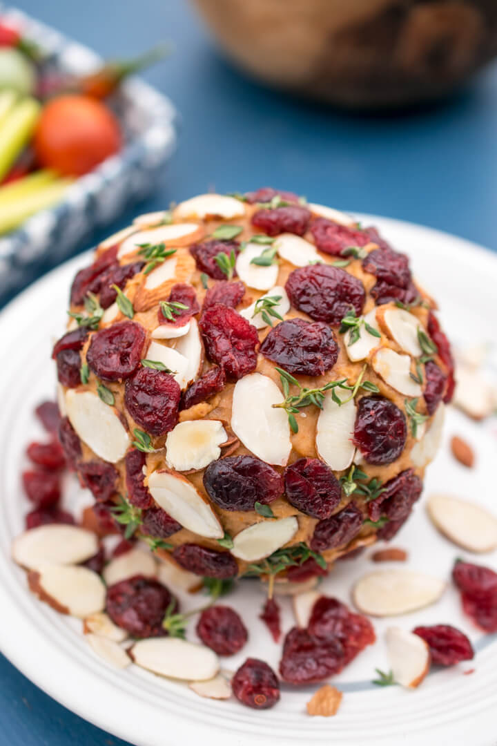 A decorated vegan cheese ball on a white plate, sprinkled with fresh thyme