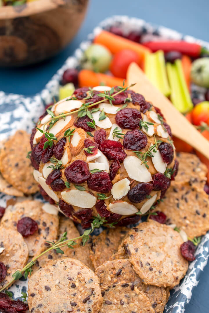 A vegan cheese ball on a ceramic platter with crackers, peppers, and cut vegetables