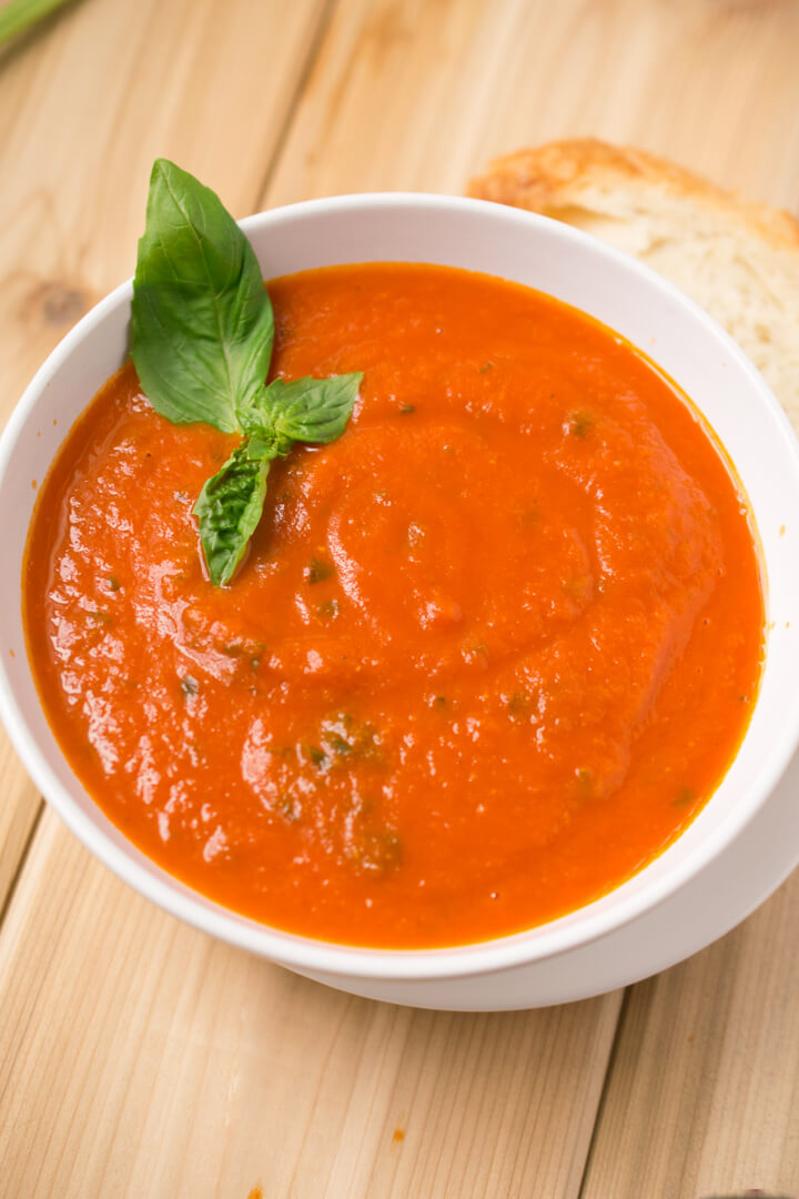 A bowl of vegan tomato soup garnished with a sprig of fresh basil.