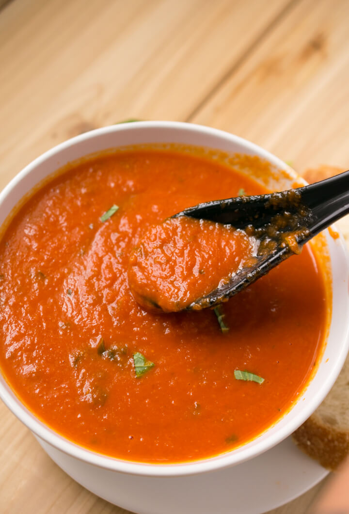 A spoonful being scooped out of a bowl of creamy vegan tomato basil soup