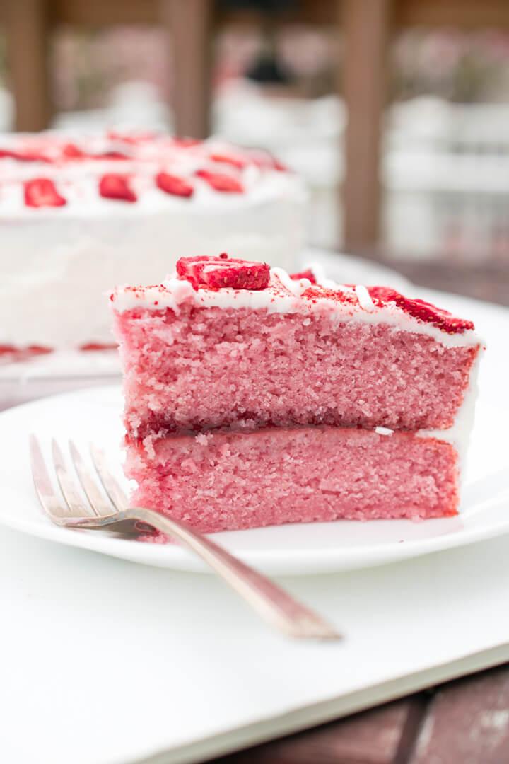 A slice of vegan strawberry cake on a white plate, with jam visible between the layers.