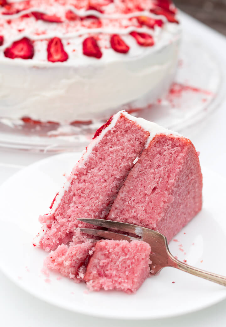 A slice of vegan strawberry cake on its side, with the rest of the cake visible in the background