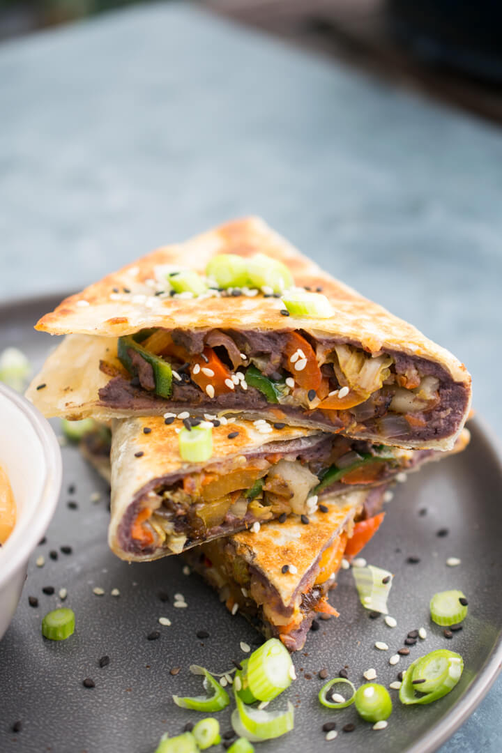 A stack of sliced vegan kimchi quesadillas on a gray plate with scallions