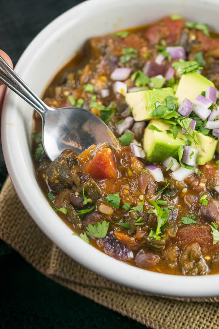 A spoon being dipped into a bowl of tomatillo black bean chili, with the texture of the tomatillos visible.