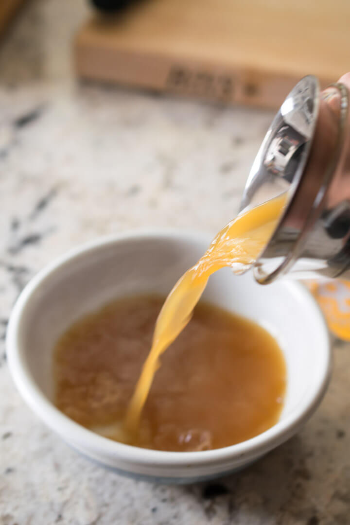 A stream of vegan beef broth being poured into a ceramic bowl