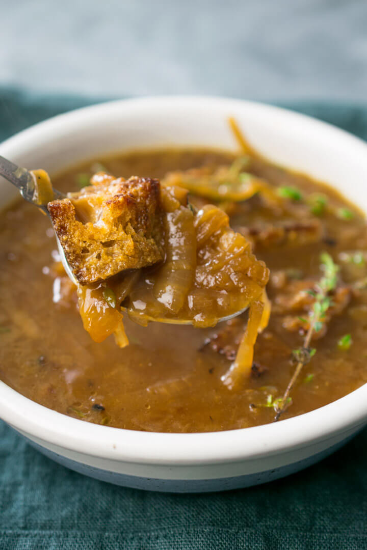 Close-up of a cheesy crouton and tender onions in a single bite of vegan French onion soup