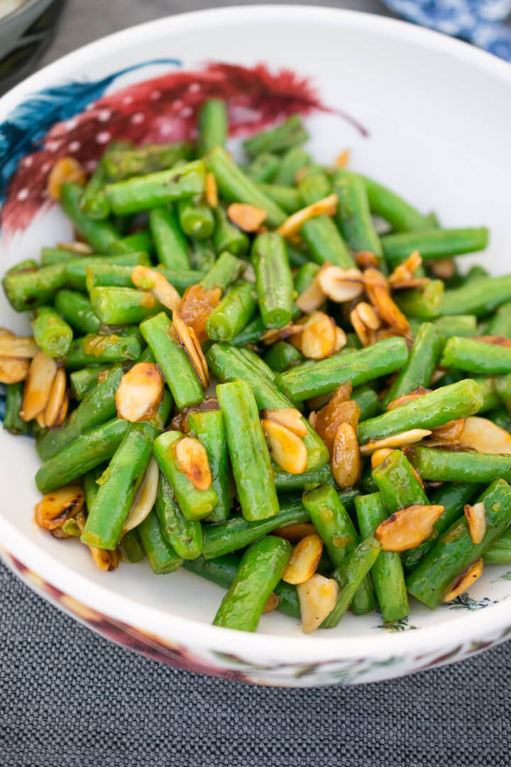 A bowl of bright green green beans with lightly browned toasted almonds.