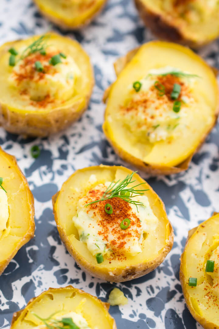 Close-up of one deviled potato, showing a creamy pale yellow filling, a garnish of a dill sprig and ground paprika